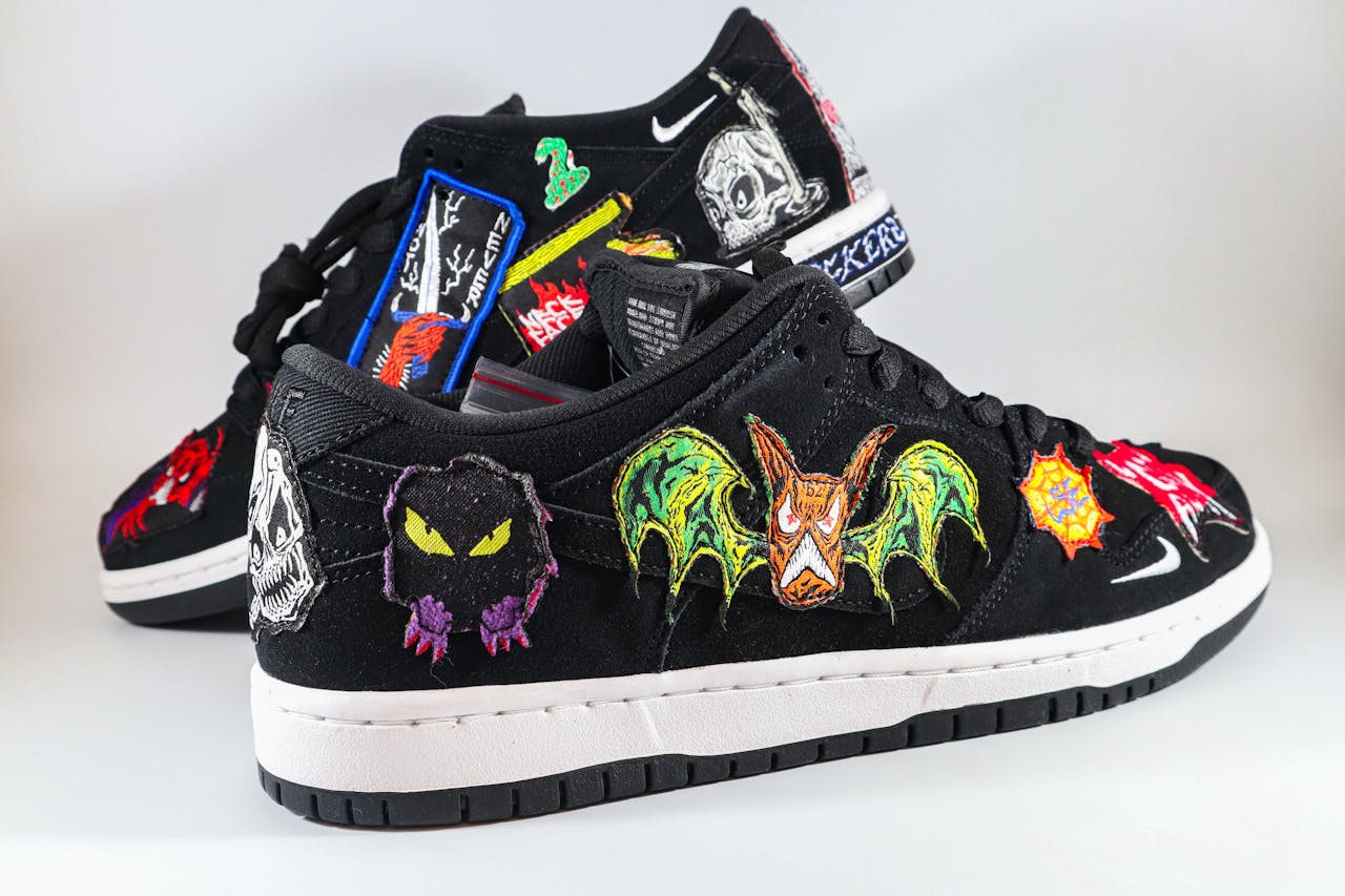 Black sneakers featuring colorful embroidered patches and unique designs on a white background.
