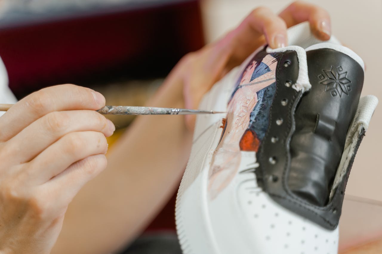 Close-up of an artist painting custom designs on a sneaker, showcasing creativity.
