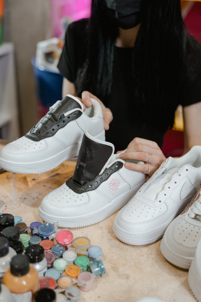 Woman customizing white sneakers with paint and brushes indoors, exploring creative designs.
